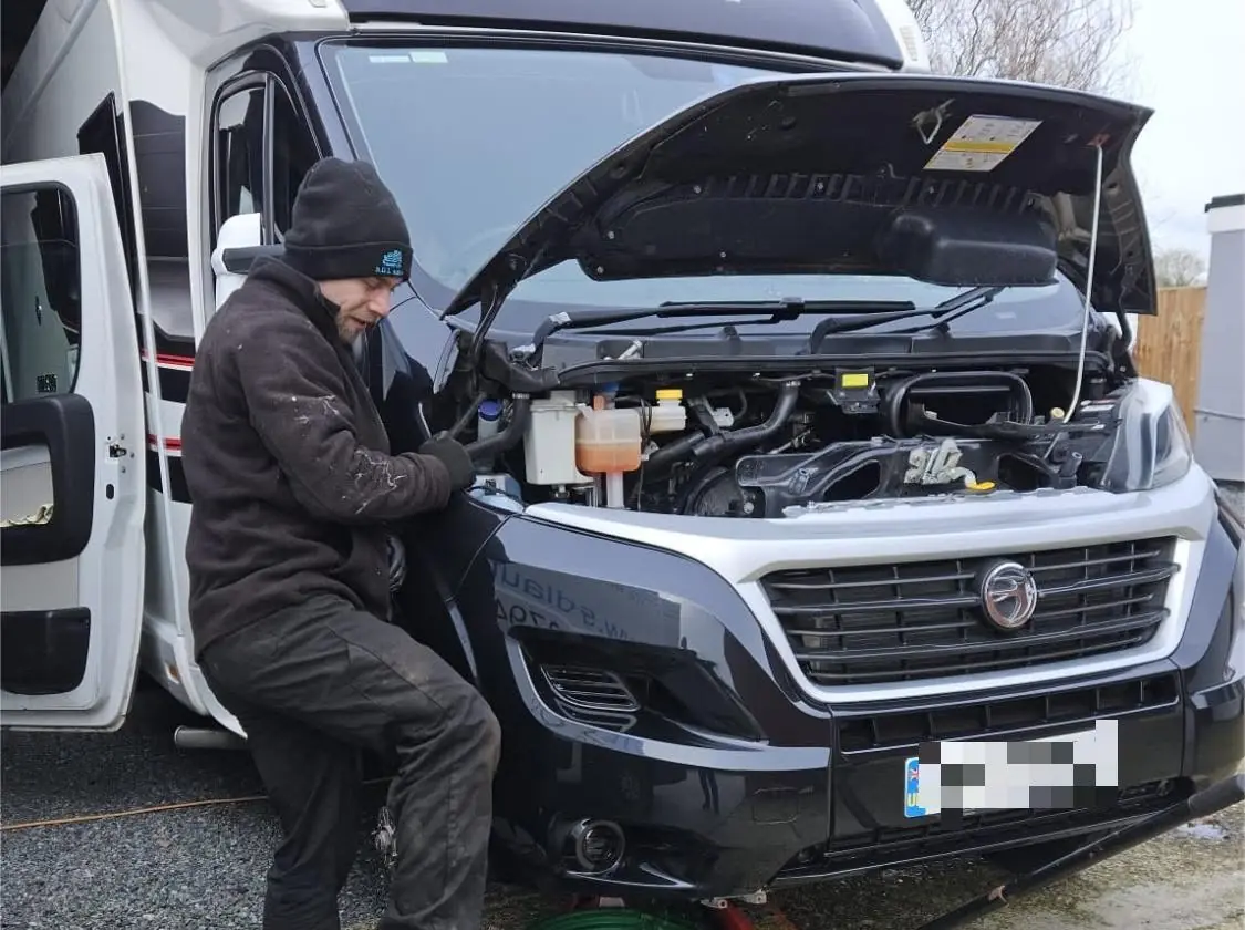 Mechanic working at the front of a Swift motorhome with the bonnet up and parts laid out on mats