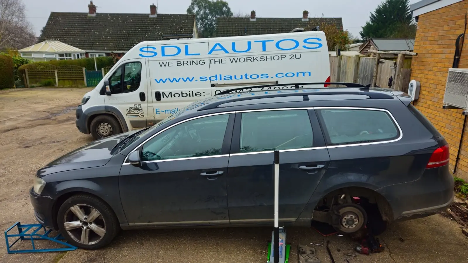 The white S.D.L Autos van, lettered We Bring the Workshop 2U, parked behind a VW Passat estate with its rear wheel off on a driveway